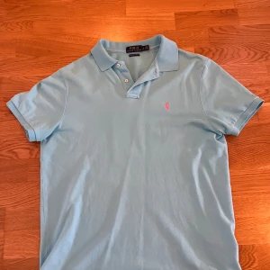 Ljusblå Piké Ralph Lauren - Snygg ljusblå polo t-shirt från Ralph Lauren med klassisk krage och två knappar framtill. Storlek L. Hör av dig vid frågor🤝