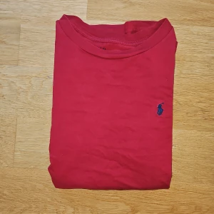 Vinröd  långärmad tröja från Polo Ralph Lauren - Säljer en vinröd långärmad tröja från Polo Ralph Lauren med klassisk rund hals och den ikoniska blå logon broderad på bröstet. Tröjan är gjord i mjuk bomull och har en enkel, clean look som funkar till jeans eller shorts.