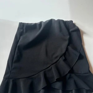 Svart volangkjol från NLY One - Supersnygg svart kortkjol från NLY One med volangdetaljer och omlott-look. Kjolen har en feminin och trendig design som passar perfekt till sneakers eller boots. Materialet är mjukt och följsamt för en bekväm passform.