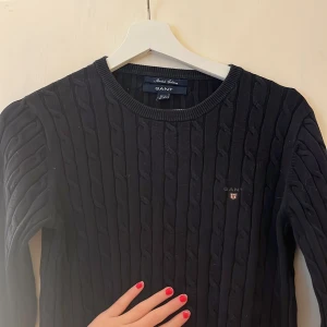 Svart Gant tröja - Kabelstickad svart tröja från GANT med rund halsringning och diskret logga på bröstet. I storlek s-m!