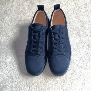 Mörkblå sneakers från Christian Louboutin - Snygga mörkblå sneakers från Christian Louboutin i mocka med signaturbroderi på hälen och ikonisk röd gummisula. Skorna har rund tå, snörning och en stilren, lyxig vibe som sticker ut med de röda detaljerna under sulan.