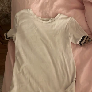 Vit t-shirt med detaljer från Zara - Vit t-shirt från Zara i storlek S. T-shirten har korta ärmar med snygga svarta och beige detaljer på ärmsluten. Den är lite smutsig, den kommer också såklart att tvättas. Jag tar en bild efter tvätten på hur den ser ut då, då pris kan diskuteras. Men en super söt gullig tshirt som passar till tex blåa jeans, svarta jeans osv!