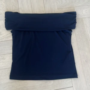 Mörkblå off shoulder från Gina Tricot - mörkblå off shoulder från Gina Tricot i enkel och stilren design. Toppen är axelbandslös och har en klassisk bandeauform som sitter tight mot kroppen. Perfekt att matcha med jeans eller kjol