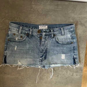 Blå lågmidjad jeanskjol från OneTeaspoon - Säljer en lågmidjad, blå jeanskjol från OneTeaspoon med slitna detaljer. Storlek 25 men måtten är (midjemått rakt över 38 cm, längd 23 cm!) Köpt second hand så vet inte om det är sydd på baksidan eller om det är designen!💙