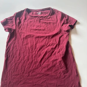 Vinröd t-shirt från 157 - En enkel vinröd t-shirt från 157 med rund hals och korta ärmar. T-shirten är gjord i mjuk bomull och har en clean look utan mönster eller detaljer. Perfekt för dig som gillar basic och stilrent.