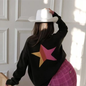 Chloe shuterman city sweater - Mörkgrön stickad tröja med rosa detaljer vid hals, ärmslut och nederkant. Stor stjärna i rosa och gult på ryggen och texten 'Los Angeles' i rosa på ena ärmen. Långärmad och loose fit, perfekt för dig som gillar statement-plagg med coola detaljer.