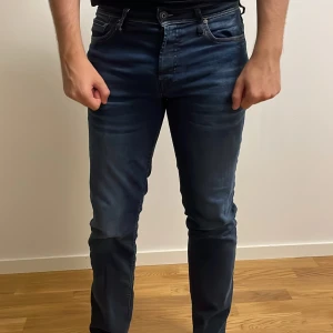 Jack & Jones Slim Straight Tim jeans - Mörkblå jeans från Jack & Jones i modellen Slim Straight Tim. Snygg tvätt med lätt slitning och klassiska gula sömmar. Jeansen har normal passform med raka ben och är tillverkade i bomull. Perfekta för dig som gillar en stilren look.