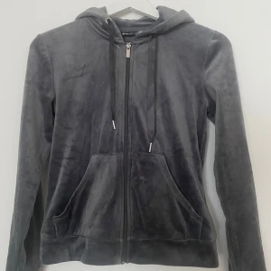 Mörkgrå velour hoodie från Gina Tricot - Säljer en mjuk och skön mörkgrå hoodie från Gina Tricot i storlek XXS. Tröjan är i velourmaterial med huva, snörning och dragkedja framtill. Den har långa ärmar och praktiska fickor på framsidan. Perfekt för chill dagar eller när du vill vara extra comfy.