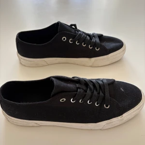 Vagabond skor - Klassiska svarta sneakers från Vagabond med vit sula och snörning. Skorna är i canvasmaterial och har en låg profil. Använda endast ett fåtal gånger med endast 1 defekt, sulan har lossnat lite vid hälen (se bild 3). Tyvärr är lådan slängd. 