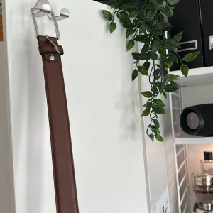 Brunt skärp från Montana i skinn - Snyggt brunt bälte från Jack and Jones med silverfärgat spänne. Klassisk design med raka kanter och diskreta sömmar längs sidorna. Perfekt accessoar för att lyfta din outfit med en stilren touch. Använder ej, för stort. 