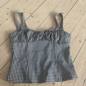 Rutig blåvit linnetopp från Zara - Supersöt rutig linnetopp från Zara i blått och vitt. Toppen har breda axelband, knytning framtill och en lätt utsvängd passform. Perfekt för varma dagar och ger en chill vintage vibe. Gjord i mjuk bomull som känns skön mot huden. Storlek M fast funkar som S