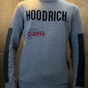 Grå sweatshirt från Hoodrich - Snygg grå sweatshirt från Hoodrich med svart tryck framtill och baktill. En liten ficka vid ena armen och få tecken på användning 