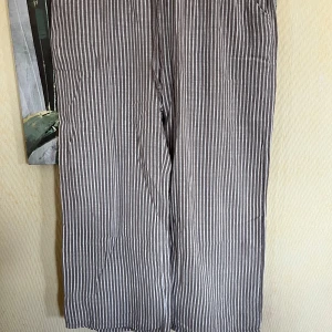 Randiga linnebyxor med snörning - Snygga randiga linnebyxor i beige och vitt med relaxed fit och breda ben. Byxorna har elastisk midja med snörning och praktiska sidfickor. Perfekta för chill dagar eller när du vill ha en luftig och skön stil.