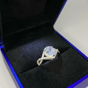 Glittrig ring i äkta silver 925s - Säljer en riktigt snygg ring i äkta silver 925s, med en stor, glittrande droppformad sten i mitten. Ringen har en cool tvinnad design med små stenar längs bandet som ger extra bling. Ej använd utan kommer från min small business.💎