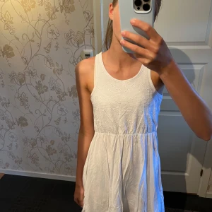 Vit sommarklänning från Pinky - Superfin vit kortklänning från Pinky med broderade blommor upptill. Ärmlös modell med rund halsringning och lätt utställd kjol. Perfekt för varma dagar och ger en fräsch och söt look.