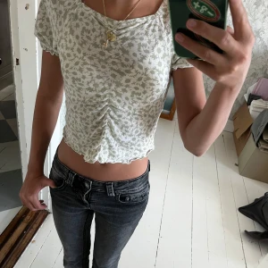 Blommig croppad blus med puffärm - Supersöt croppad blus med ljusgrönt blommönster på vit botten. Toppen har korta puffärmar, rynkdetalj framtill och vågig kant nertill. Perfekt för sommarens alla dagar och ger en romantisk vibe till din outfit. ( barn storlek 146-152)