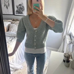 Ljusgrön stickad kofta med knappar - Superfin ljusgrön stickad kofta med v-ringning och stora vita knappar framtill. 