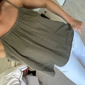 Olivgrön linnetopp med tunna axelband - Säljer en olivgrön linnetopp med tunna axelband och avslappnad passform. Toppen har rynkade detaljer vid halsringningen och är tillverkad i ett lätt och luftigt material, perfekt för varma dagar. Enkel och stilren design som är lätt att matcha.