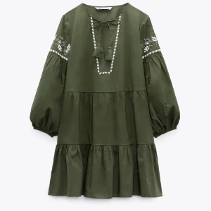 Grön broderad kortklänning från Zara - Supersöt grön kortklänning från Zara med vita broderade detaljer och volang. Klänningen har v-ringning med knytband, ballongärmar och blommigt broderi på ärmarna. Perfekt för sommarens alla äventyr!