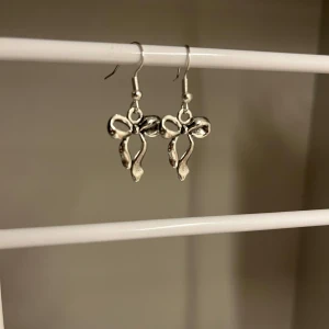 Silvriga örhängen med rosettform - Supersöta silvriga örhängen i form av rosetter. Hängande modell som ger en gullig och trendig vibe till din look. Perfekta för dig som vill ha något unikt och lekfullt i smyckesamlingen. Handgjort 