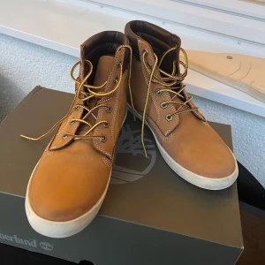 Bruna Timberland boots i skinn - Snygga bruna boots från Timberland i skinn med vita sulor och klassiska gula snören. Skorna har högre skaft, vadderad brun kant och robust design. Perfekta för dig som gillar streetstyle och vill ha något som sticker ut.Jättefin skick