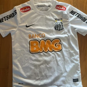 Vit Santos Neymar Jr matchtröja Nike - Santos FC fotbollströja i vitt med Neymar Jr och nummer 11 på ryggen. Nike Dri-FIT material, kortärmad modell med klubbmärke, sponsorer och svarta detaljer. Snygg och klassisk design för fans av brasiliansk fotboll.