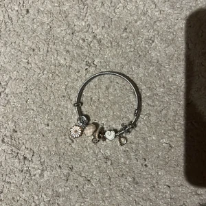 Silverfärgat armband med berlocker - Fett Snyggt armband i silverfärg med flera berlocker💓💓 bland annat en blomma, ett hjärta, en bokstav och pärlliknande detaljer. Armbandet har en modern och personlig stil med inslag av vitt och guld på vissa berlocker😚 Perfekt accessoar för att lyfta din outfit!!😍😍