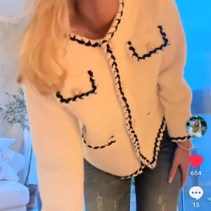 Vit cardigan jacka  - Supersnygg vit cardigan jacka med svarta detaljer längs kanterna och fickorna. Jackan har fyra fickor framtill, pärlknappar och en klassisk rund halsringning. Perfekt för dig som vill ha en chic och trendig look.