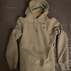 Biege Morris hoodie (ny) - Snygg beige hoodie från Morris med liten broderad logga på bröstet och patch på ärmen. Tröjan har huva med snörning och ribbade muddar. Perfekt för dig som gillar stilren och enkel design. Tillverkad i mjuk bomullsmix för maximal komfort. Storlek är S men är lite oversized så passar medium, krymper man i torktumlare får man medium. Den är sprillans ny och aldrig använd då morsan köpte fel storlek o ryckte lappen. Nypris är 1500kr. Pruta går.