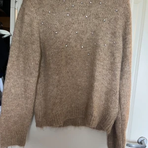 Beige stickad tröja med pärlor Stories - Supermysig beige stickad tröja med pärldetaljer upptill. Tröjan har lång ärm, rund hals och en lite fluffig känsla. Perfekt för dig som gillar en chill men ändå snygg look. Kommer ej ihåg var den är ifrån men endast testad. Storlek s