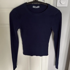 Mörkblå långärmad topp från New Yorker - Säljer en mörkblå långärmad topp från New yorker i stretchig bomull. Modellen är tight och har rund halsringning. Perfekt att styla med jeans eller mjukisbyxor för en chill look. Enkel och stilren design utan mönster eller detaljer.