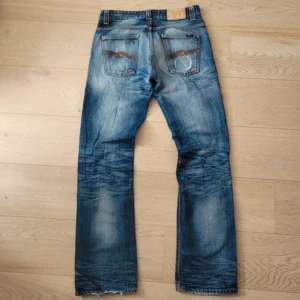 Vintage Ola Bootcut Nudie Jeans med slitningar - Säljer ett par riktigt snygga vintage Nudie jeans i modellen Bootcut Ola. Riktigt schysst tvätt med naturliga slitningar. Skön passform med klassisk bootcut. De är 30W/34L i storleken. Ytterbenslängd: 107 cm. Midja (tvärs över): 40 cm. Benöppning: 21,5 cm.