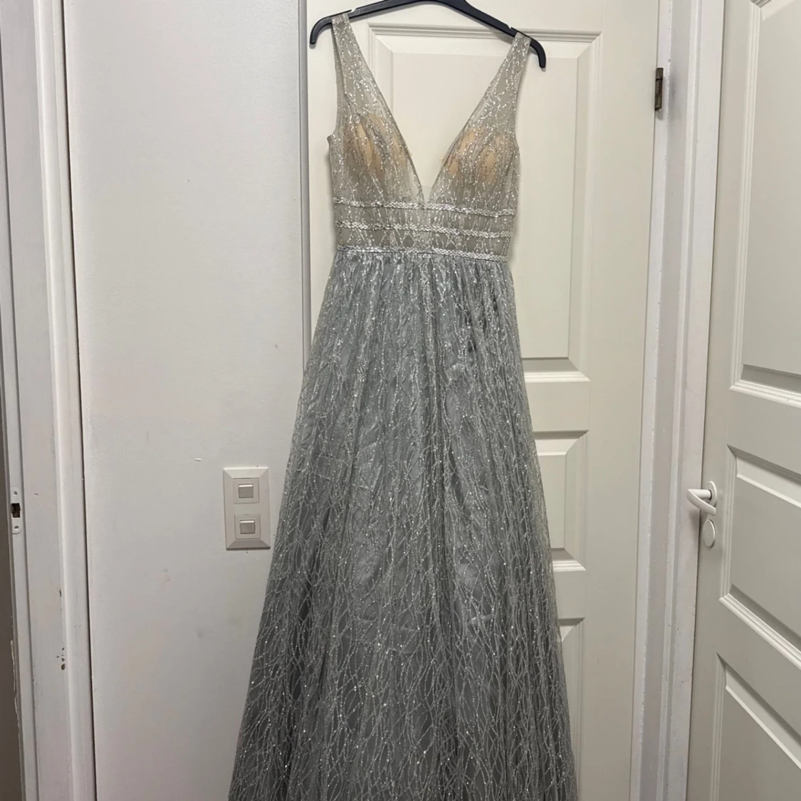 Kimalteleva hopeanvärinen pitkä mekko, jossa syvä v-pääntie