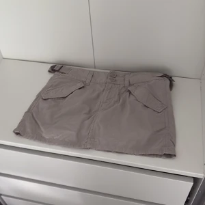 beige cargo kortkjol med fickor - snygg beige kortkjol med två stora fickor framtill. kjolen har knäppning med två knappar.
