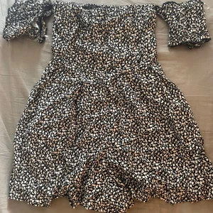 Blommig offshoulder kortklänning - Supersöt svart kortklänning och små vita blommor. Offshoulder-modell med elastiska ärmar. Ny skick! 