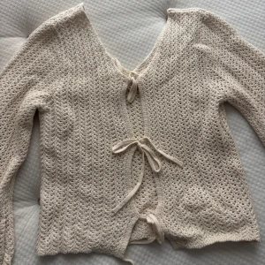 Beige stickad kofta med knyt - Supersöt beige stickad kofta med lång ärm och v-ringning. Helt oanvänd, passar både XXS och XS. Koftan har fina knytband framtill och ett luftigt, virkat mönster som ger en chill och trendig vibe. Perfekt att slänga över ett linne eller klänning för en extra touch. 