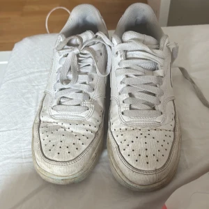 Vita Nike sneakers - Klassiska vita Nike sneakers i skinn med perforerad tå och snörning. Swoosh-logga på sidorna och Nike-tryck på hälen. Platt sula och låg modell, perfekt för en clean streetstyle-look.