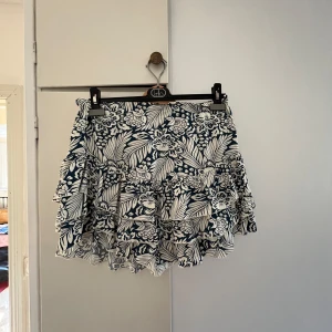 Blommig volangkjol i blått och vitt - Supersöt kort kjol med blå och vitt blommönster och flera volanger. Kjolen har en flowy känsla och elastisk midja som gör den bekväm och lätt att bära. Har tyvärr inte kommit till användning..