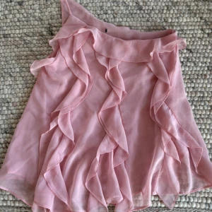 Rosa volang topp med oneshoulder - Säljer denna fina  rosa topp med volanger och oneshoulder-design från zara. 🩷 använd få gånger, skriv för fler bilder!
