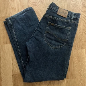 Mörkblå Lee jeans straight fit - Snygga mörkblå jeans från Lee med klassisk femficksdesign och raka ben. Jeansen har Lee-logga på bakfickan och läderpatch i midjan. Perfekta för dig som gillar en tidlös och clean look.