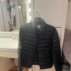 Mörkblå pufferjacka med dragkedja - Snygg mörkblå pufferjacka med hög krage och horisontella sömmar. Jackan har dragkedja framtill och två fickor på sidorna. Perfekt för kyliga dagar och enkel att matcha med olika outfits.