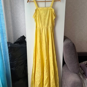 Gul långklänning med blommönster - Lång gul klänning i glansigt tyg med subtilt blommönster. Klänningen har axelband, rak urringning och medföljande bolero. Snygg detalj med dragkedja i sidan!💞Köpt secondhand, skulle tippa på strl S-M