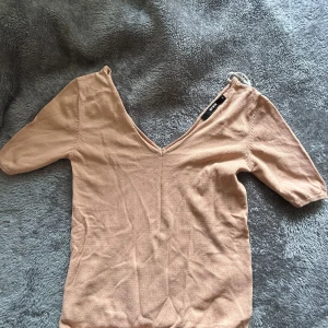 Beige v-ringad topp från Bik Bok - Säljer en beige topp från Bik Bok med v-ringning och halvlånga ärmar. Toppen har en enkel och stilren design i mjukt material, perfekt att matcha med jeans eller kjol. Passformen är normal och färgen är varm beige.