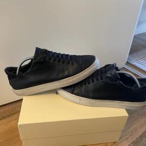 Svarta sneakers från Axel Arigato - Stilrena svarta sneakers från Axel Arigato i skinn med klassisk vit sula. Lågt skaft, rund tå och svarta snören ger en clean look. Perfekta för dig som gillar minimalistisk design och vill ha ett par snygga skor till vardags.