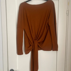 Rostbrun långärmad topp från Vila - Säljer en snygg rostbrun långärmad topp från Vila med knytdetalj framtill. Jättebra kvalitet, tröjan har endast använts 2 gånger. Storlek XS, men passar även S. 