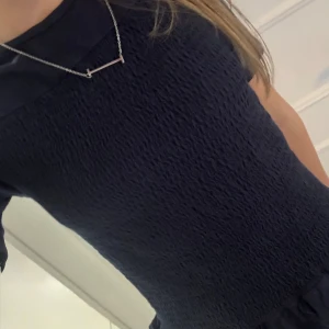 Mörkblå smockad topp med volang - Supersöt mörkblå topp med smockat tyg och volangkant nertill. Kortärmad och figurnära passform som ger en trendig look. Perfekt att styla med jeans eller kjol för en cool vibe. Är i xs men stretchig 🤍