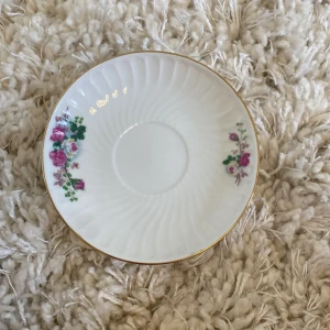  En porslinte kopp  Med en liten tallrik till -  En vit porslin kopp med en liten tallrik till med fina rosa blommor på .