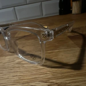 Chrome hearts - Snygga glasögon med transparent båge och rektangulär form. Sidorna har guldiga metallinslag och blommönster som ger en unik touch. Perfekta för dig som vill sticka ut med stilrena men ändå iögonfallande accessoarer.