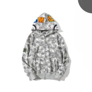Grå camo zip hoodie från Bape - Säljer en grå camo hoodie från Bape med dragkedja och broderade färgglada bokstäver på huvan. Jackan har ribbade muddar, fickor och patch på ärmen. Perfekt för dig som gillar streetwear och vill sticka ut.