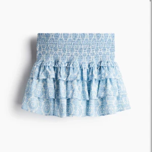 Blå volangkjol från H&M Divided - Supersöt kort volangkjol från H&M i ljusblått och vitt med blommigt mönster. Kjolen har smock i midjan och flera lager volanger för extra fluffig känsla. Perfekt för sommarens alla tillfällen och har inbyggda shorts under!! Helt nya använda en gång🩷